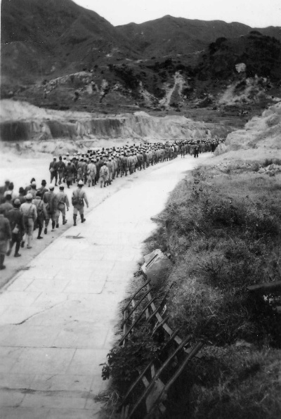 Japanese POWs are marched to work at Kai Tak Airport, in this case building new offices, other structures and a perimeter fence